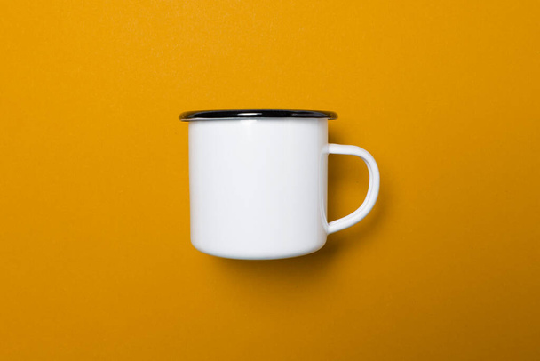 One white enamel cup with a black rim on a yellow uniform background, light an soft shadows, use es virtual meeting background or template - Фото, изображение