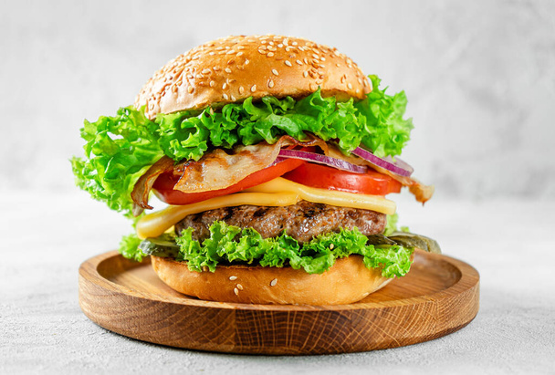 Концепция американской еды. Бургер с говядиной и беконом на деревянной тарелке на сером бетонном фоне. - Фото, изображение