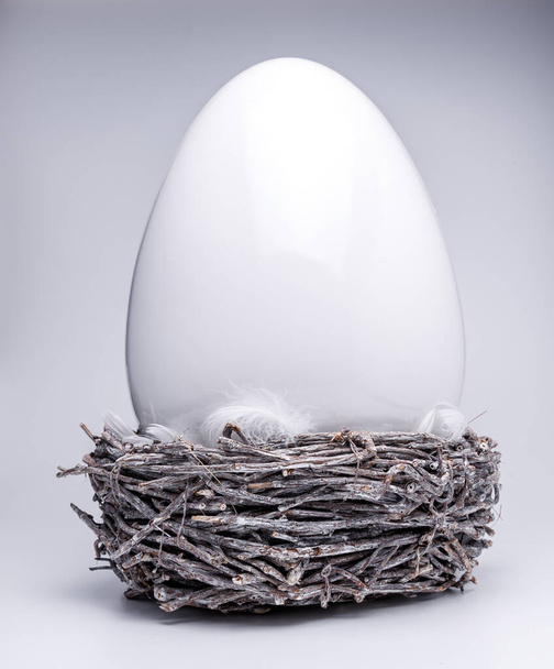un huevo de Pascua de cerámica grande en nido de Pascua gris marrón con plumas blancas, Pascua creativa y decoración de primavera 2021, colores de tendencia sobre fondo aislado blanco - Foto, imagen
