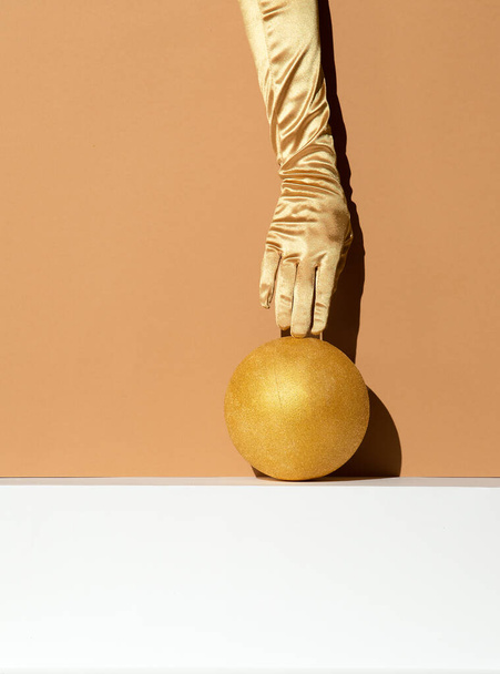 Hand in golden gloves holding ball. Abstraction minimal still life. Holiday, christmas concept - Zdjęcie, obraz