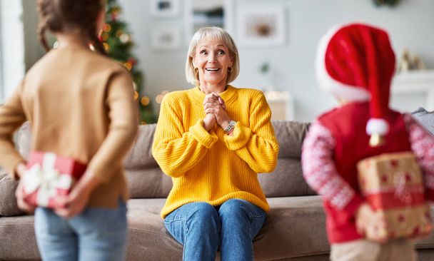 happy family grandchildren gives a cheerful smiling surprised grandmother a Christmas gift at hom - Foto, Bild