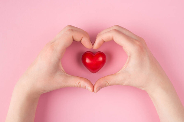 Topo acima pontos gerais primeira pessoa vista de perto foto de mãos em forma de coração e um coração vermelho isolado no fundo cor-de-rosa pastel com copyspace - Foto, Imagem
