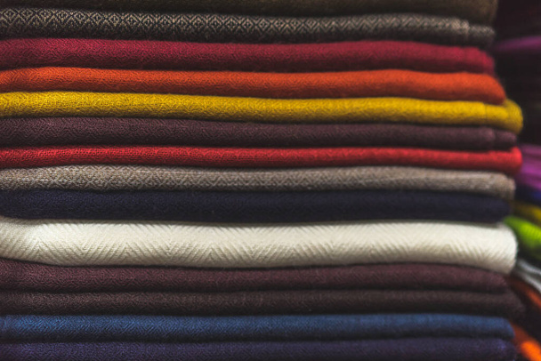 крупным планом разноцветной ткани, кучей кашемирового текстиля, стопкой разноцветной одежды, кучей одежды, темными красками шарфов - Фото, изображение