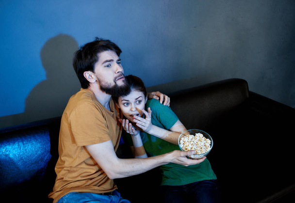 Φίλοι άντρες και γυναίκες βλέπουν τηλεόραση στον καναπέ και ποπ κορν σε πιάτο. - Φωτογραφία, εικόνα