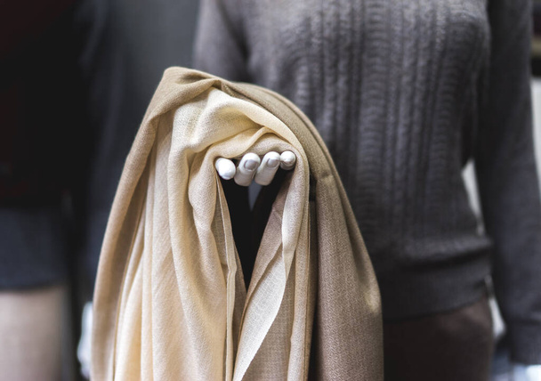A mannequin with light beige cashmere fabric in hand. Natural pashmina clothing. Woollen shop. close up of a person holding a scarf - Photo, Image