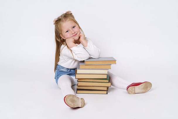 Education and people concept. Portrait of a teenage girl who sits near the books, leaning on them. Isolated over white background. - Foto, Imagen