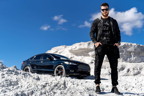 Attractive guy in fashion clothes travels by auto. Luxury car and white rocks background. Stylish young male. - 写真・画像