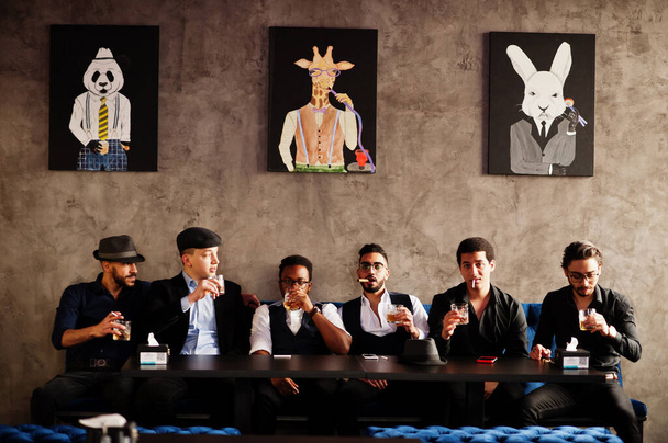 Group of handsome retro well-dressed man gangsters spend time at club, sitting and drinking whiskey. Multiethnic male bachelor mafia party in restaurant. - Photo, image