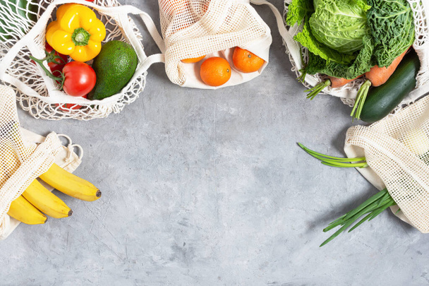 Friss zöldségek és gyümölcsök tote környezetbarát táskák szürke asztal tetejére néző. Öko vásárlási koncepció. Egészséges nyers evés. - Fotó, kép