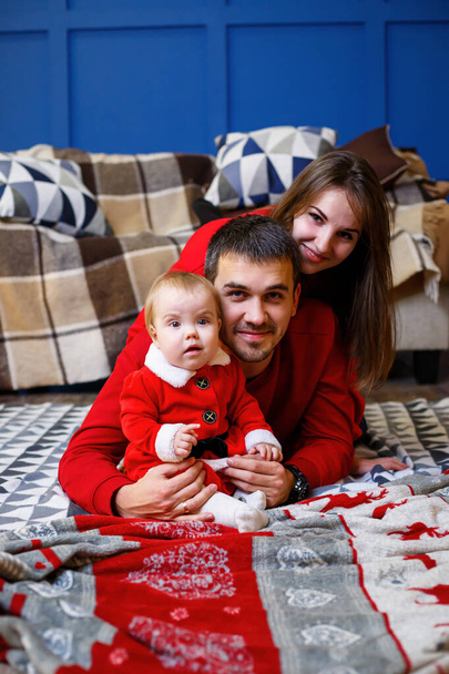赤いセーターの幸せな家族が床に一緒に座っています。クリスマス休暇の雰囲気。サンタの衣装を着た子供。家族関係の概念 - 写真・画像