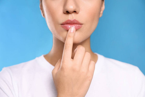 Woman with herpes touching lips on light blue background, closeup - Foto, afbeelding