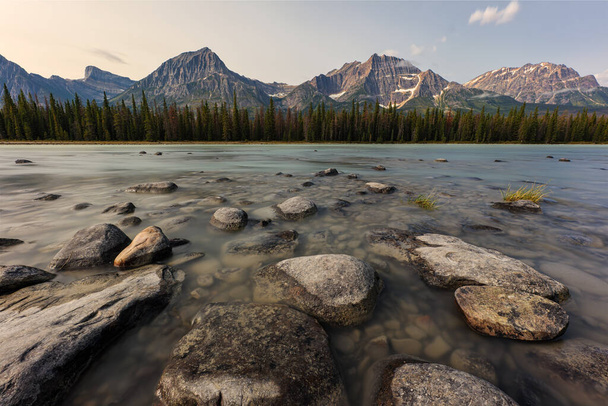 Rocks on a River with forest and Mountains in the background along the Icefields Parkway in Jasper National Park, Alberta, Kanada. - Valokuva, kuva
