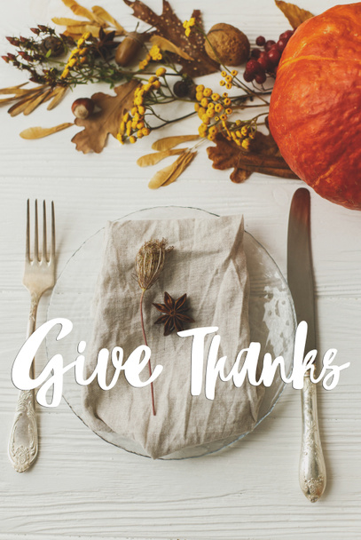 Happy Thanksgiving greeting card. Give Thanks text handwritten on thanksgiving table setting, plate, linen, anise, autumn leaves, pumpkin, autumnal flowers on white table. Seasons greetings - Foto, afbeelding