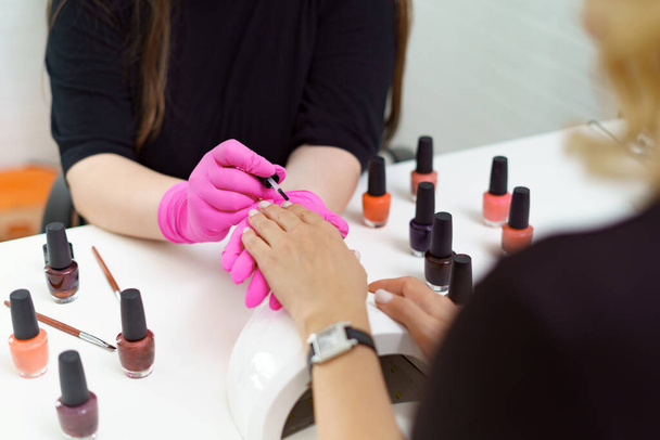 Manicurist treating client at beauty nails salon. Manicure, painting on nail - Фото, изображение