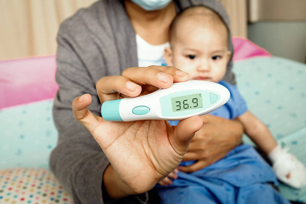 Asiática mamá sostiene un termómetro digital Medir su hijo, Enfoque en la mano - Foto, Imagen