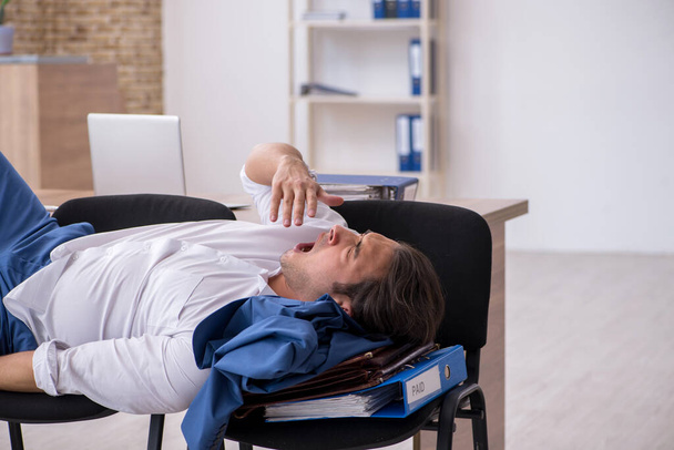 Jonge mannelijke werknemer slapen in het kantoor op stoelen - Foto, afbeelding
