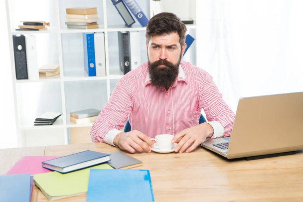 Brutal hipster with serious look drink coffee at agent desktop in modern office, employee - Foto, afbeelding