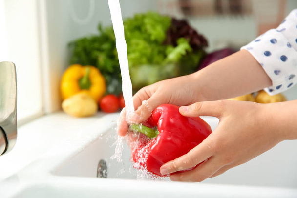 Woman washing fresh red bell pepper in kitchen sink, closeup - Foto, immagini