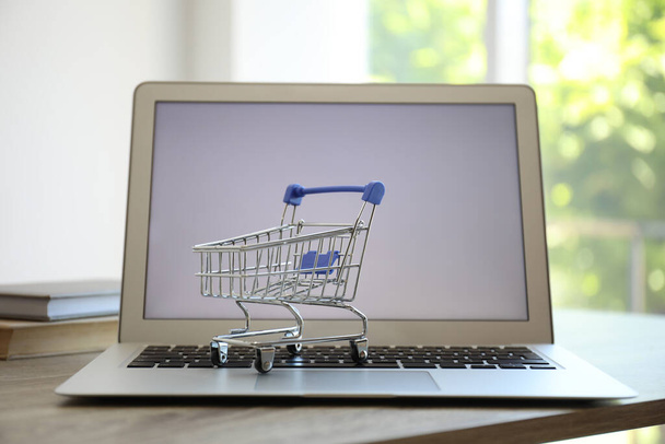 Internet shopping. Laptop with small cart on table indoors - 写真・画像