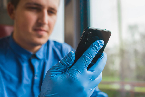 Chlap v ochranných lékařských rukavicích drží telefon a tráví v něm čas, zblízka - Fotografie, Obrázek