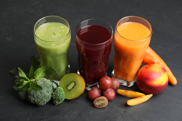 Delicious colorful juices in glasses and fresh ingredients on black table - Fotó, kép
