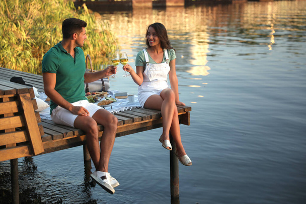 Couple clinking glasses with wine on pier at picnic - Photo, Image