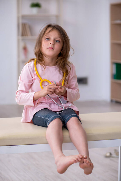 Small girl holding stethoscope waiting for doctor in the clinic - Foto, imagen