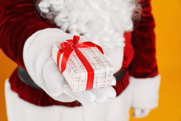 Santa Claus holding Christmas gift on yellow background, closeup - Foto, immagini
