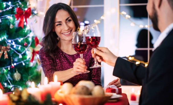 Happy beautiful elegant couple in love are sitting at christmas table and drinks wine from glasses. - Foto, Imagem