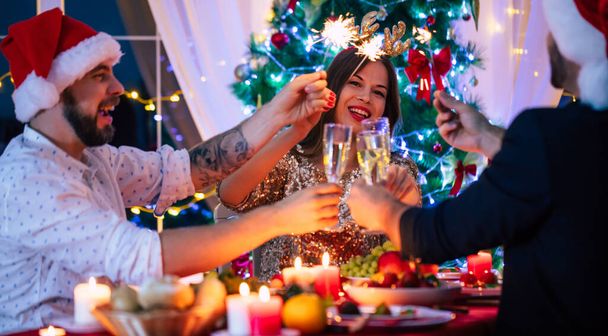 Group of happy excited beautiful friends while they are eating with glasses wine in hands at a home christmas party and having fun. - Zdjęcie, obraz