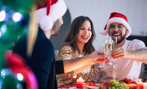 Groep van gelukkige opgewonden mooie vrienden terwijl ze eten met glazen wijn in handen op een home christmas party en plezier hebben. - Foto, afbeelding
