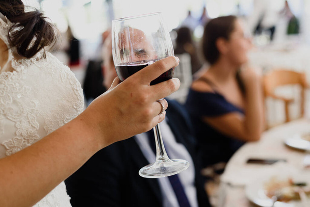 Το χέρι μιας νύφης κρατά ένα ποτήρι κρασί έτοιμο να μεθύσει.. - Φωτογραφία, εικόνα