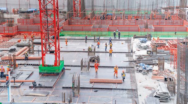 The  employee wearing safety uniform working in the construction site with red cranes and steel pillar for build modern residential area, construction concept for the develop city. - Photo, Image