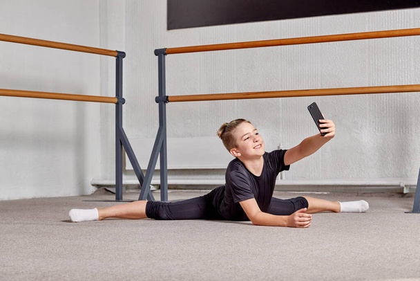 A young man lies on the floor on the splits in the gym and takes a selfie. - Zdjęcie, obraz
