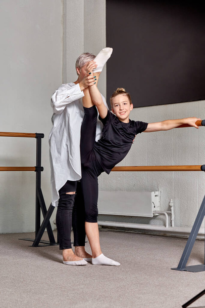 A teacher teaches a man ballet. Lift your leg high up, flexibility training. - Фото, изображение