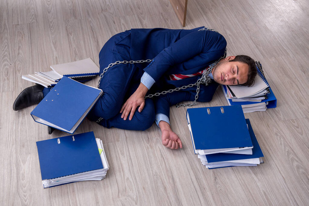 Geketende mannelijke werknemer ongelukkig met overmatig werk in het kantoor - Foto, afbeelding