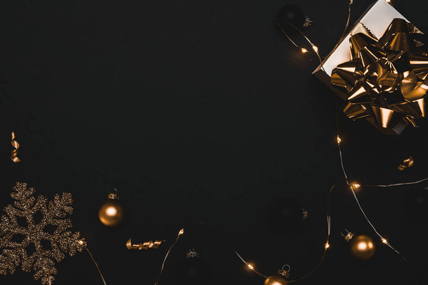 Счастливого Рождества. Белый подарок с золотым луком, золотые шары и блестящие гирлянды огни в рождественской украшения на темном фоне для поздравительной открытки. Рождество, зима, концепция нового года - Фото, изображение