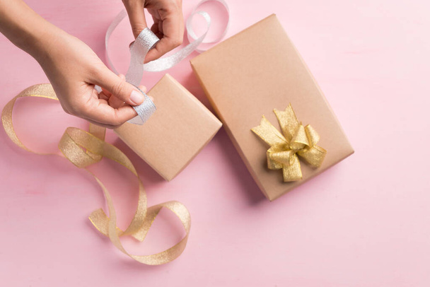 Caja de regalo de papel decorada con plata y cinta dorada de la mano de la mujer, embalaje presente para dar en día especial, vista superior - Foto, imagen