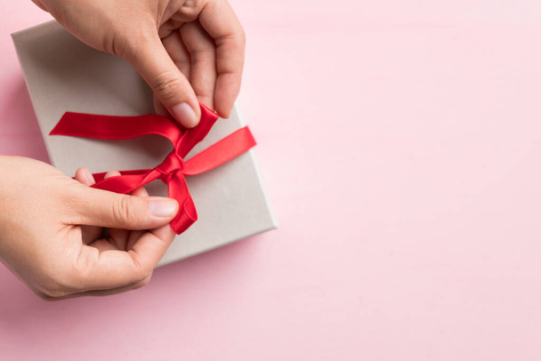 Χάρτινη συσκευασία δώρου διακοσμημένη με κόκκινη κορδέλα από γυναικεία χέρια, Συσκευασία δώρου για προσφορά σε ξεχωριστή μέρα, Top view - Φωτογραφία, εικόνα
