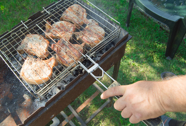 Κοντινό πλάνο ενός άνδρα χέρι προετοιμασία τηγανητό κρέας, σε εξωτερικούς χώρους, το καλοκαίρι, με φόντο το γρασίδι - Φωτογραφία, εικόνα