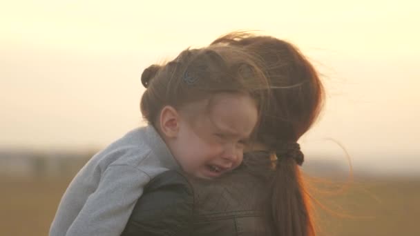 Dziecko płacze w parku w ramionach mamy. Mamusia uspokaja dziecko. rodzina matka i dziecko ze łzami w oczach przytula matkę, emocjonalnie. kochający młody matka przytula i łagodzi jej mało - Materiał filmowy, wideo