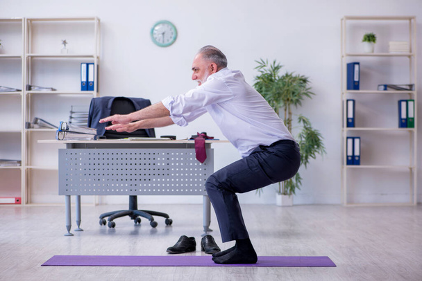 Verouderde mannelijke werknemer doet fysieke oefeningen tijdens de pauze - Foto, afbeelding