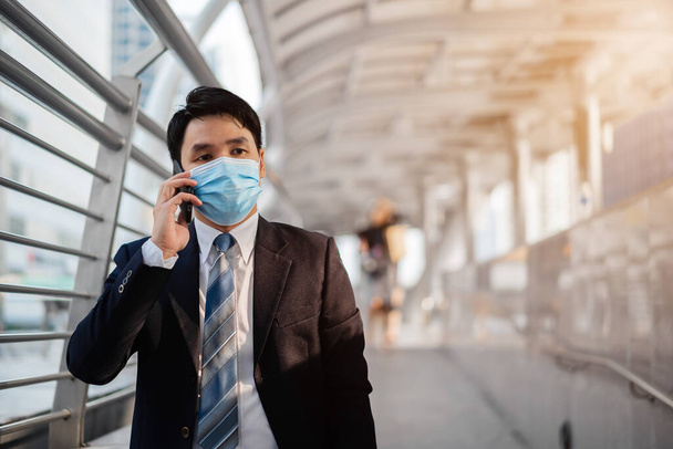obchodní muž mluví na mobilním telefonu a nosí lékařskou masku během pandemie koronaviru (covid-19) ve městě - Fotografie, Obrázek