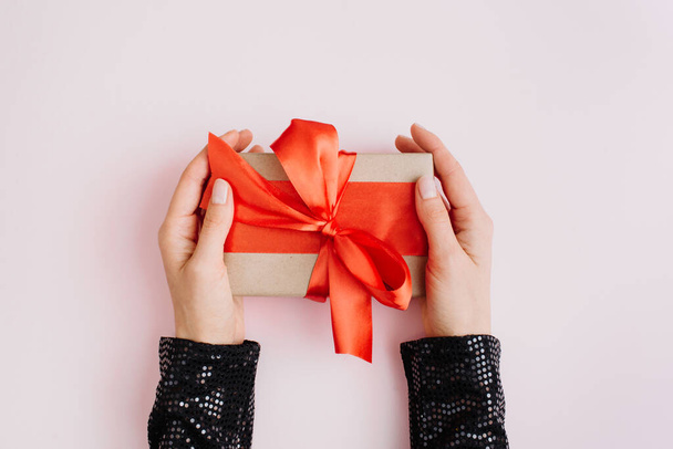 Woman hands holding present box with red bow on pastel pink background. Flat lay, top view, copy space. - 写真・画像