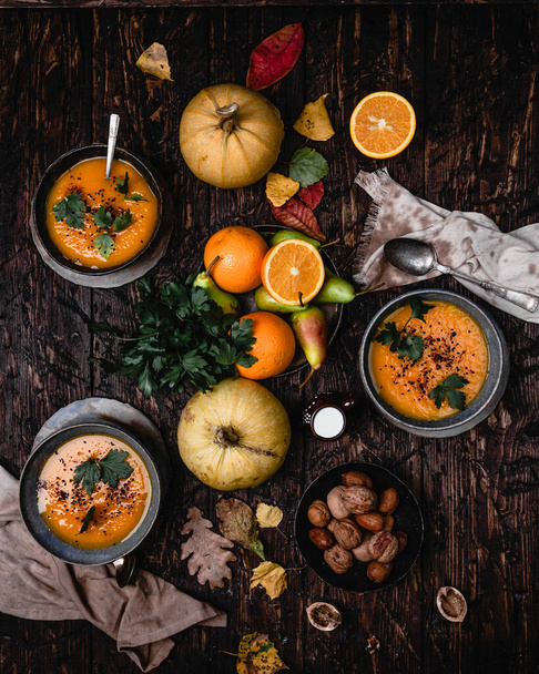 pumpkin soup in bowls with fresh vegetables and fruits on rustic wooden background. - Foto, afbeelding