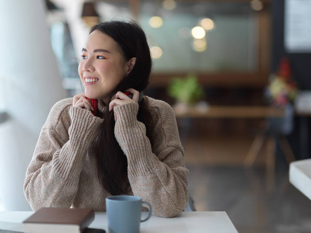 Retrato de mujer joven en suéter auriculares blancos relajante mientras lee libro en la cafetería - Foto, imagen