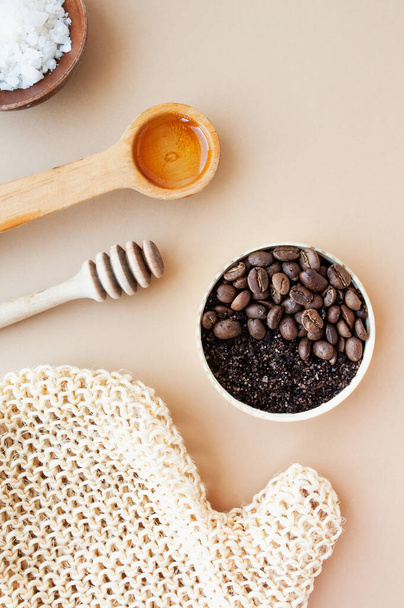 Καφές scrub και κόκκους καφέ σε χρυσό βάζο, μέλι, καλλυντικό λάδι και ξύλινο ραβδί για το μέλι σε παστέλ μπεζ φόντο, καλλυντικά σπιτιού, καλλυντική διάταξη αντι-κυτταρίτιδα προϊόντα, επιλεκτική εστίαση - Φωτογραφία, εικόνα