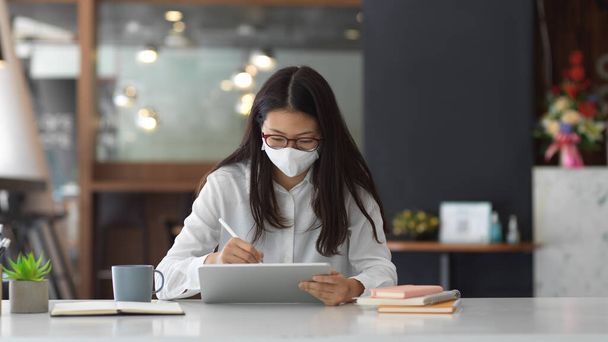 Portrait of female office worker wearing mask while working in office - Фото, изображение