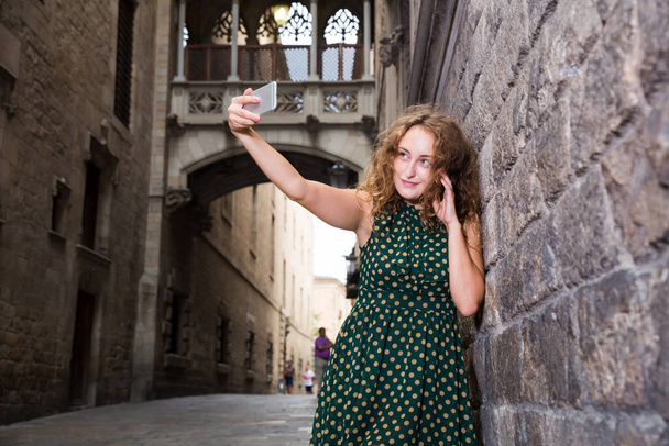 Cheerful young girl standing near brick wall and making selfie with phone - Foto, Imagem