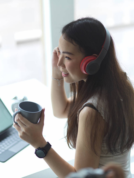 Portrét dospívající ženy ve svetru si udělat přestávku na kávu, zatímco sedí na pracovišti - Fotografie, Obrázek